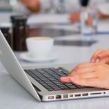 Close up of assistant using laptop, writing meeting informations while doctors discussing in background during medical conference sitting at desk in hospital office. Profesional team brainstorming